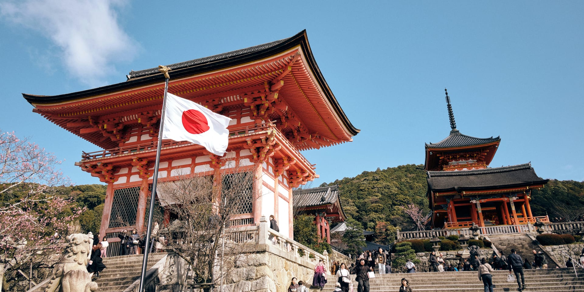 Cherry blossoms framing Kiyomizu-dera temple gate with a Japanese flag, Kyoto
